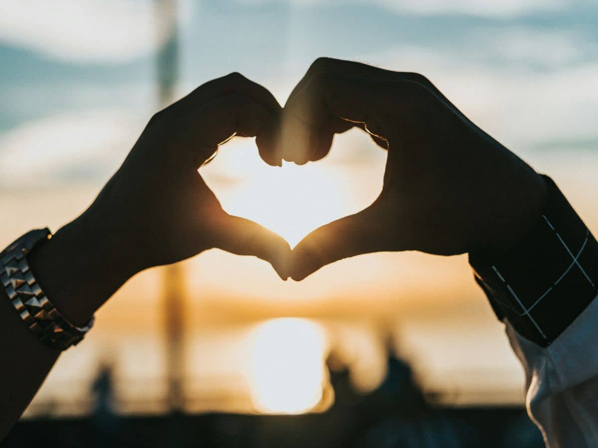 two hands creating heart shape with sun in background