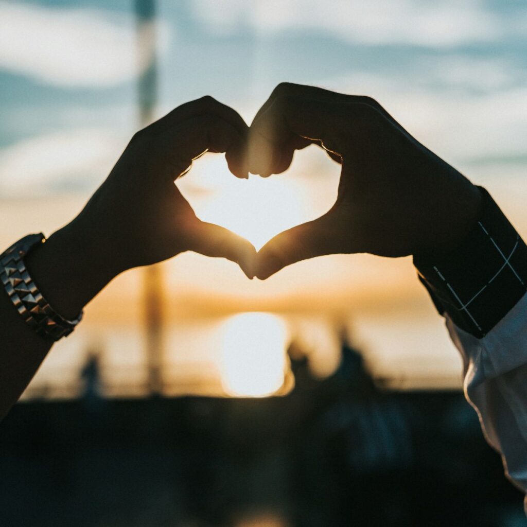 two hands creating heart shape with sun in background